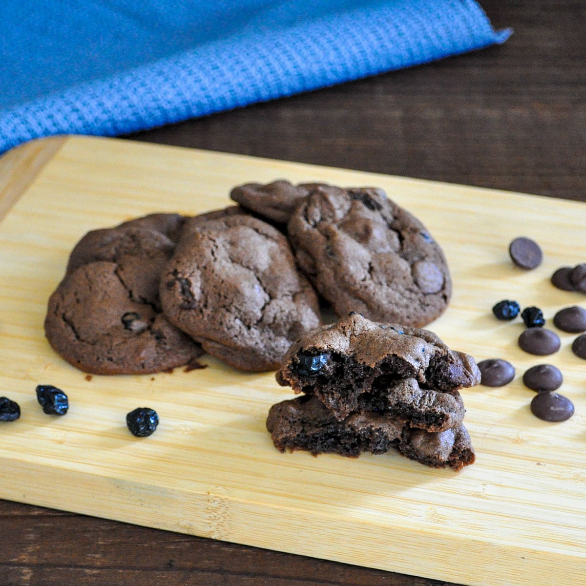 chocolate cookies with dried blueberries and chocolate chips sitting on a bamboo board