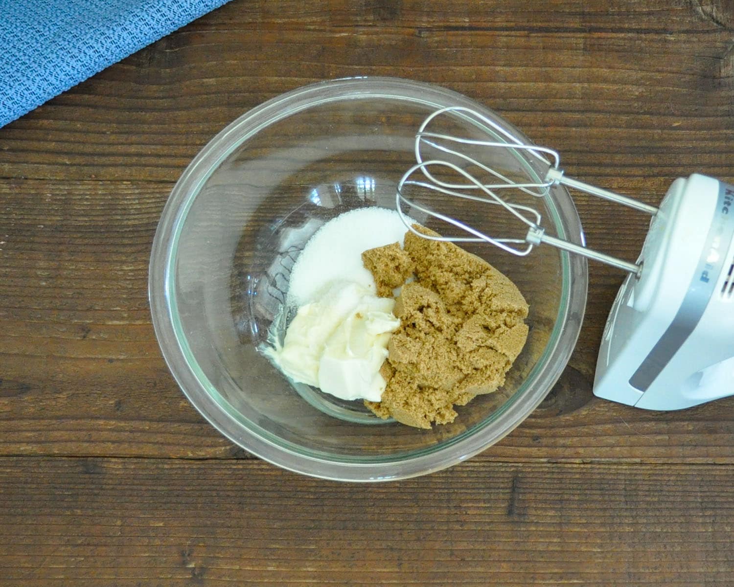 butter, granulated sugar, brown sugar in a glass bowl next to a kitchen aid mixer ready to be mixed