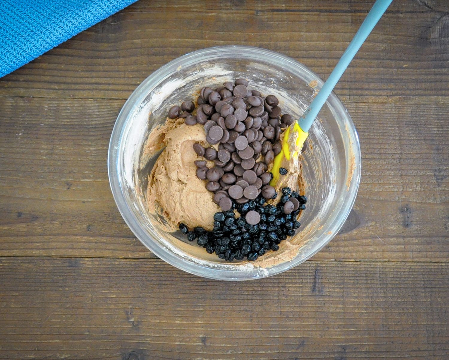 chocolate chips and dried blue berries added to chocolate cookie dough in a glass bowl