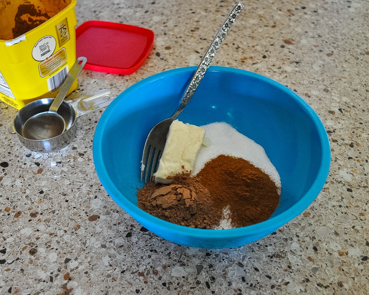 cocoa powder, sugar, butter, and cinnamon in a blue bowl ready to be mixed together