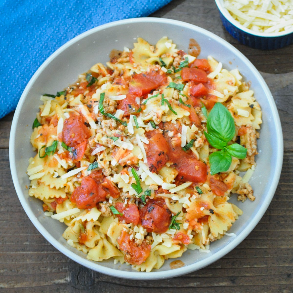 pasta, ground turkey, tomatoes in a gray bowl topped with basil and parmesan cheese