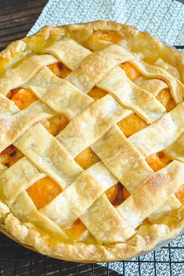 A fresh apricot pie with lattice topping sitting on a black wire rack.