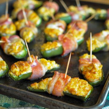 a baking sheet filled with bacon wrapped stuffed jalapenos