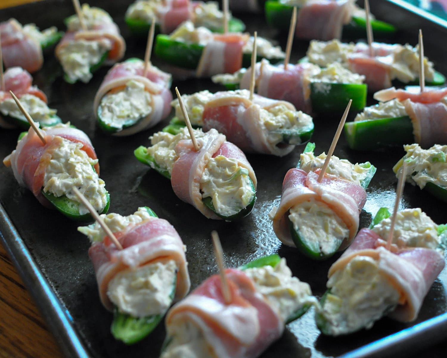 a baking pan with stuffed jalapenos wrapped in raw bacon