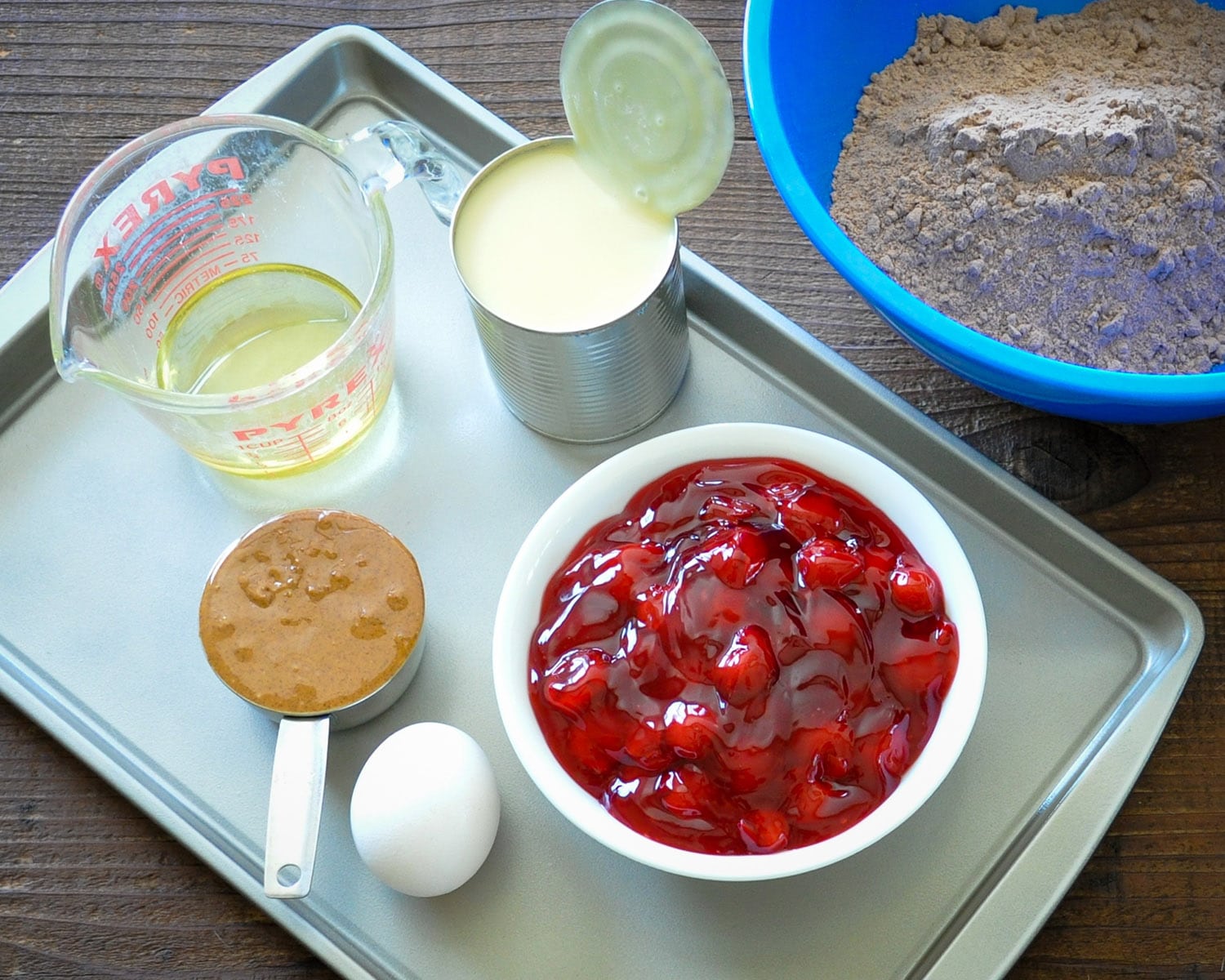 overhead picture of an egg, brown sugar, oil, condensed milk, cherries, and a chocolate cake mix