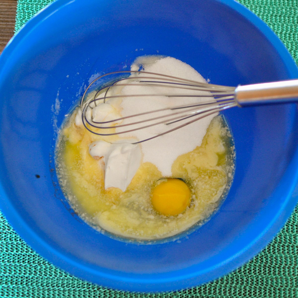 sugar, egg, yogurt and vanilla in a blue bowl with a whisk