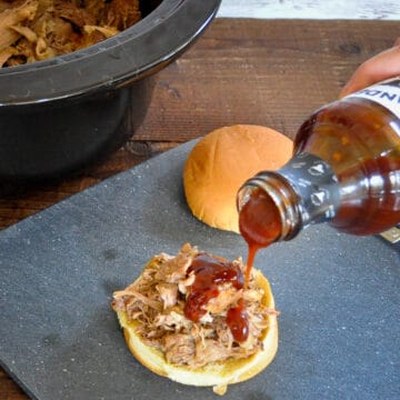 shredded pork on a bun with bbq sauce being poured on top