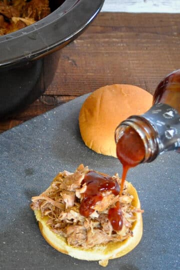 shredded pork on a bun with bbq sauce being poured on top