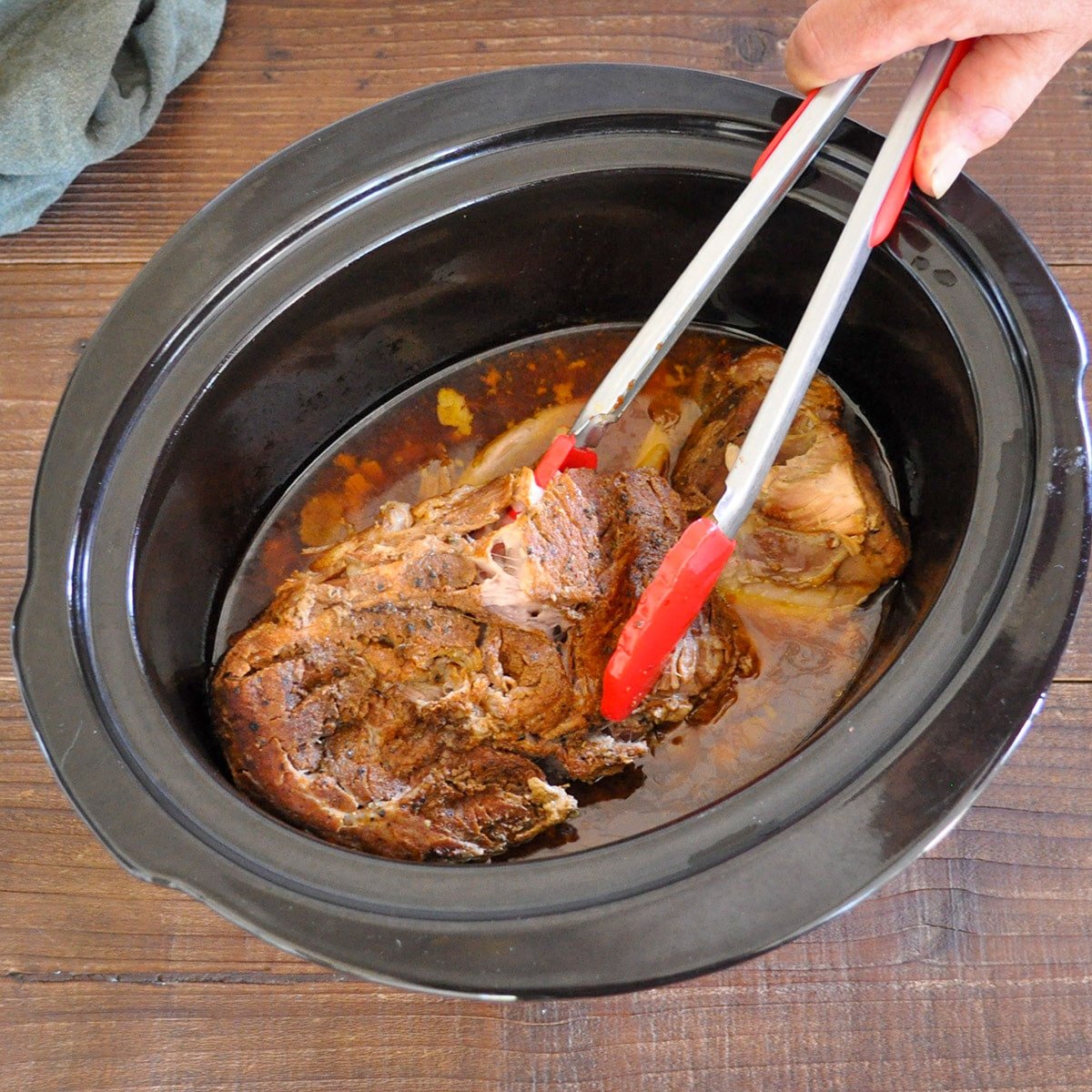 pork butt in a crock pot that has finished cooking being lifted with red tongs