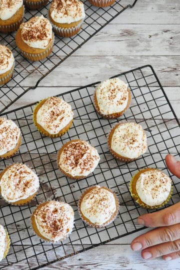Finished tiramisu cupcakes being served on a black wire rack.