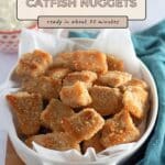 A white dish filled with golden Baked Catfish Nuggets, with a green cloth and dipping sauce in the background—perfect for trying your favorite baked catfish nuggets recipe.