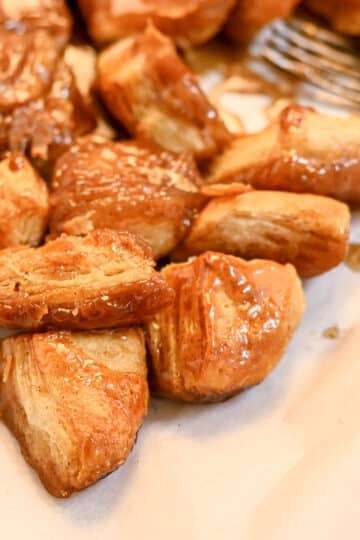Close-up of sticky biscuit pieces flipped onto parchment paper, glossy with cinnamon brown sugar caramel.