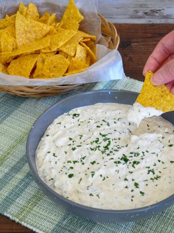 a bowl of tortillas next to a bowl of dip with someone dipping a chip