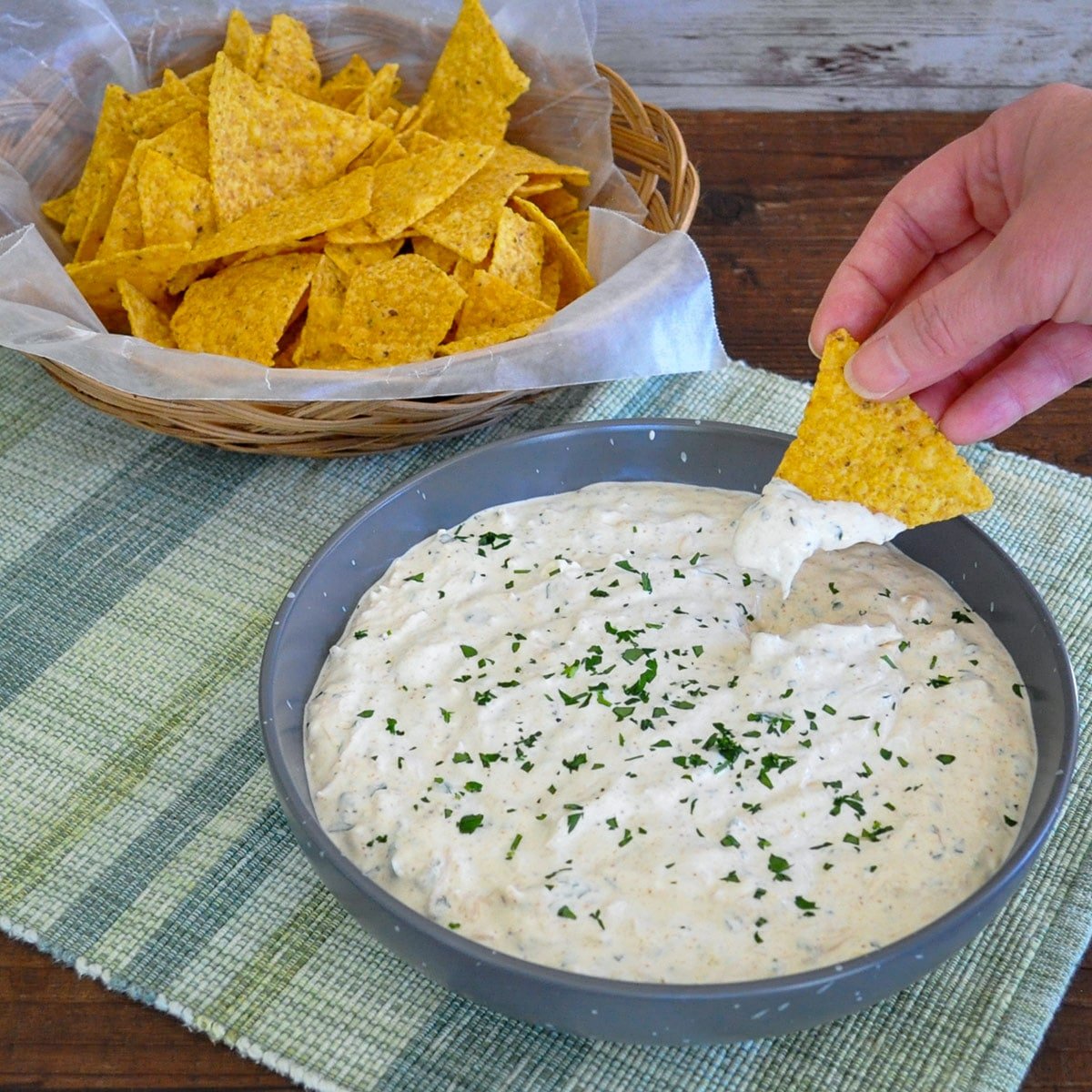 a bowl of tortillas next to a bowl of dip with someone dipping a chip