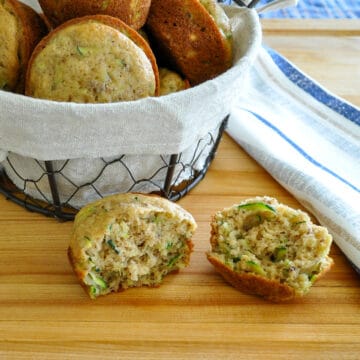 a split open zucchini muffin next to a basket of muffins