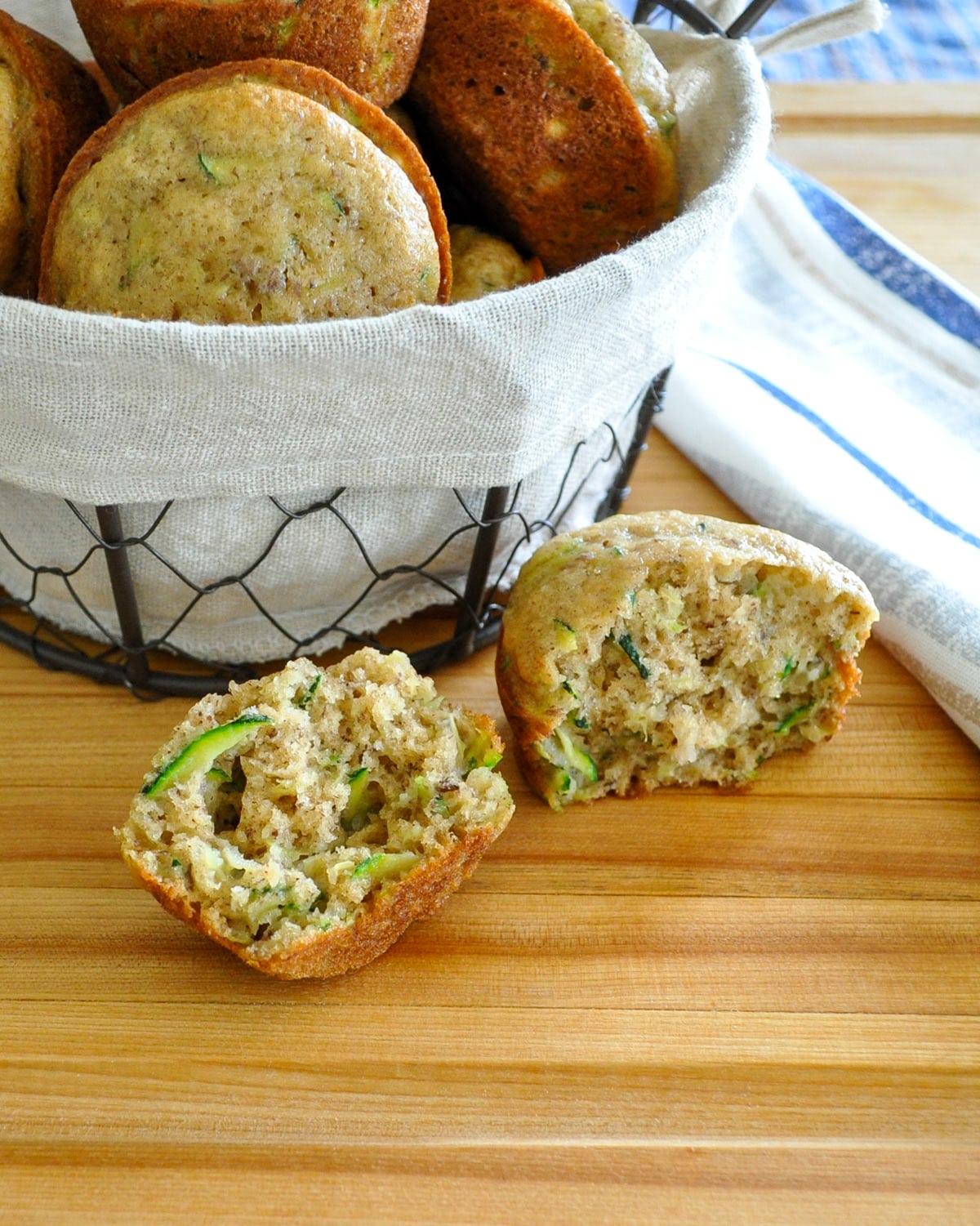 a split open zucchini muffin next to a basket of muffins