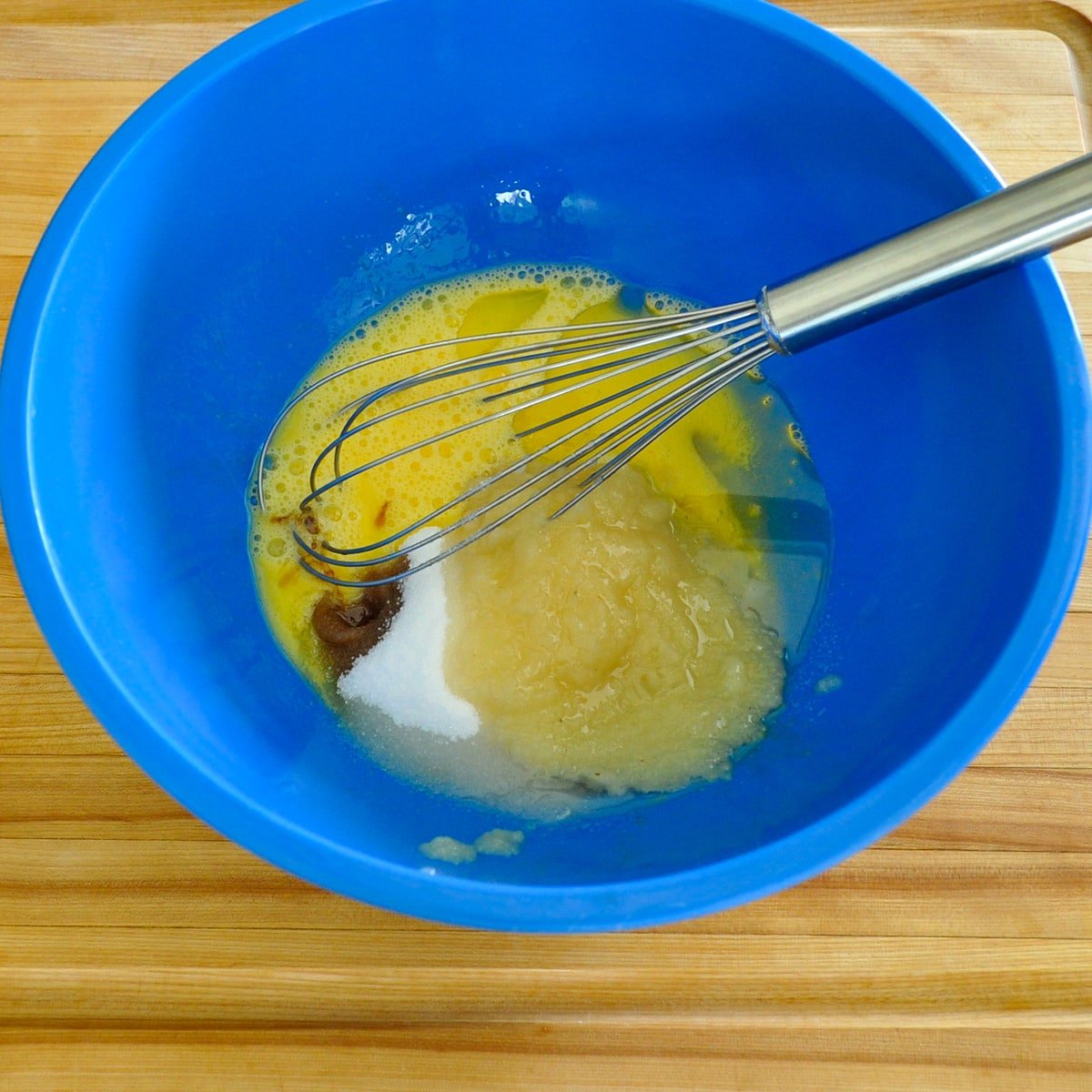 Beaten eggs with sugar, oil, applesauce, and vanilla in a blue bowl