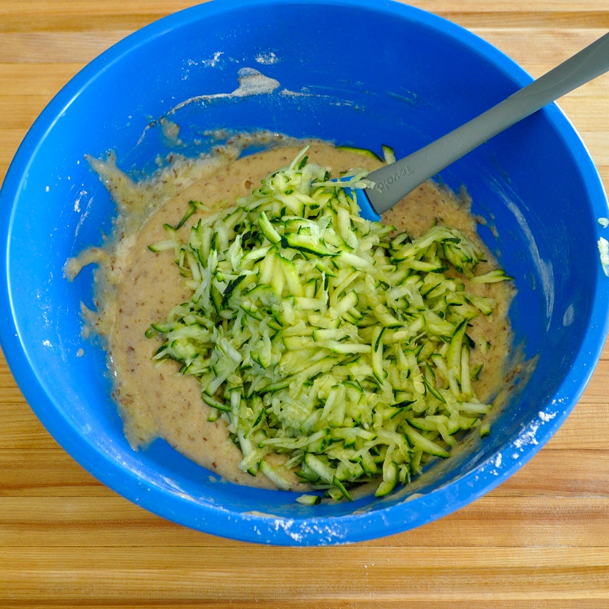 Zucchini ready to mix in to muffin batter in a blue bowl