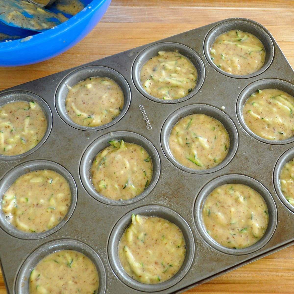 a muffin pan filled with zucchini muffins batter ready to bake