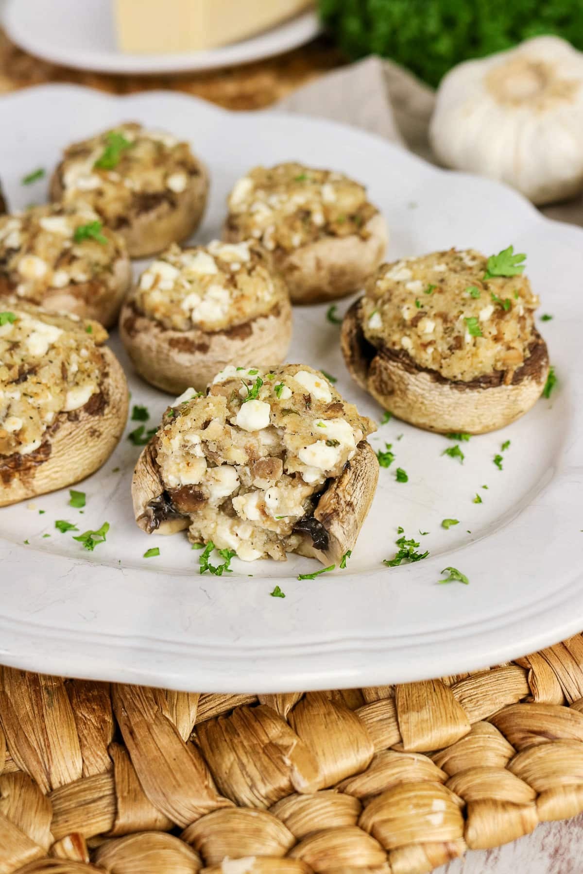 Easy Stuffed Mushrooms with crumbled cheese and herbs are served on a white plate, garnished with chopped parsley.
