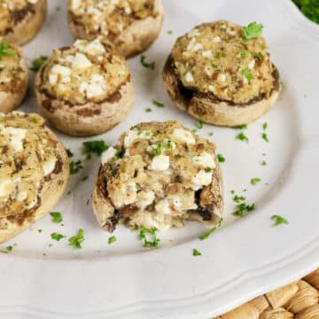 Easy Stuffed Mushrooms topped with herbs and cheese, arranged on a white plate with a fresh parsley garnish.
