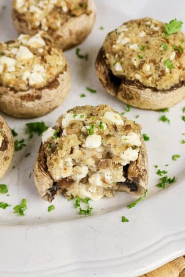 Easy Stuffed Mushrooms topped with herbs and cheese, arranged on a white plate with a fresh parsley garnish.