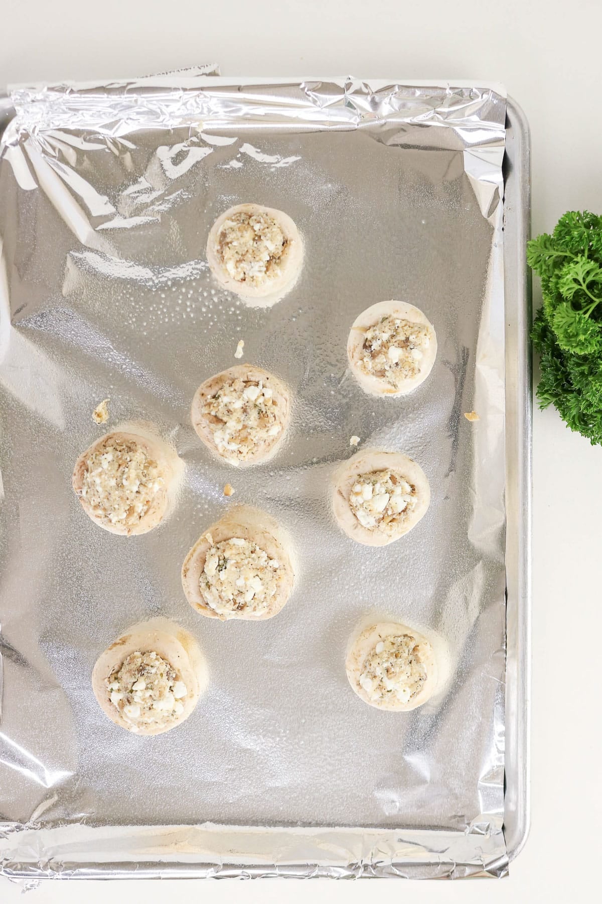Eight Easy Stuffed Mushrooms rest on a foil-lined baking sheet, garnished with fresh parsley on the side.
