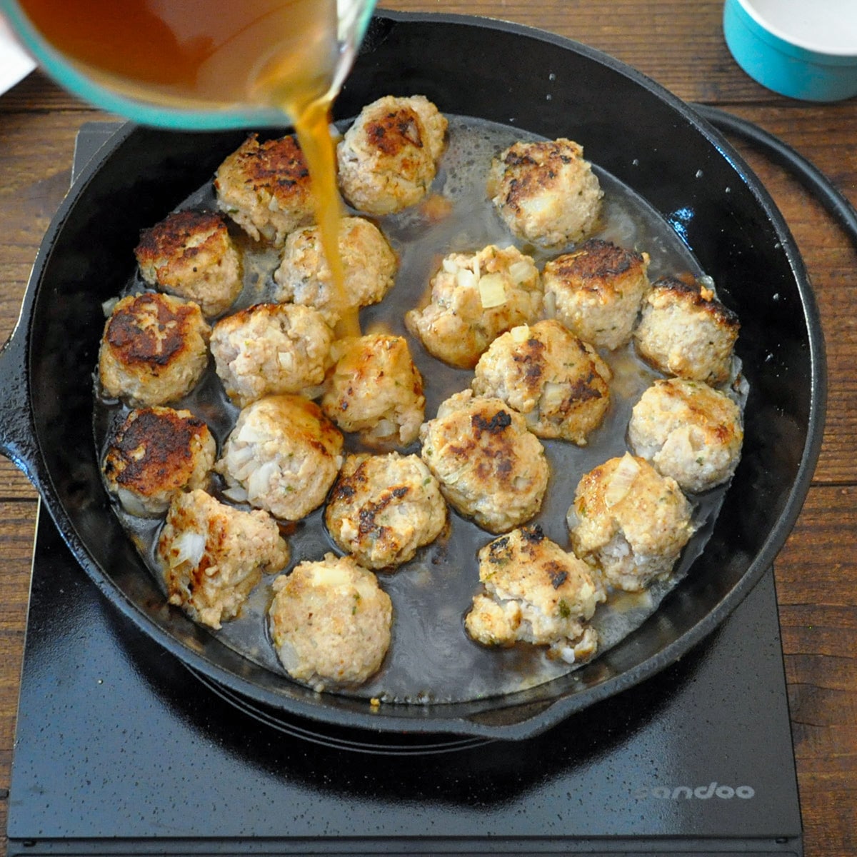 beef broth being poured over meatballs in a black skillet