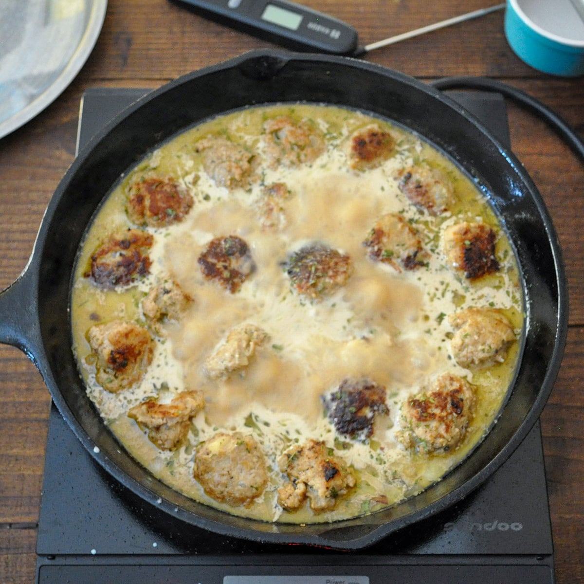 meatballs cooking in broth and cream in a cast iron skillet