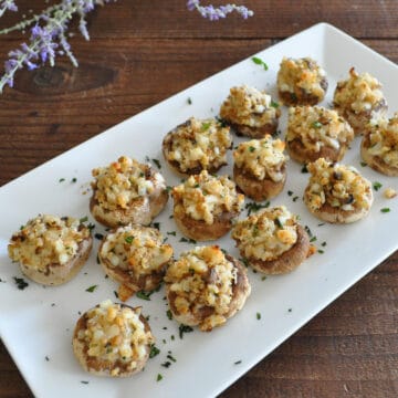 stuffed mushrooms on a white platter next to a bundle of lavendar