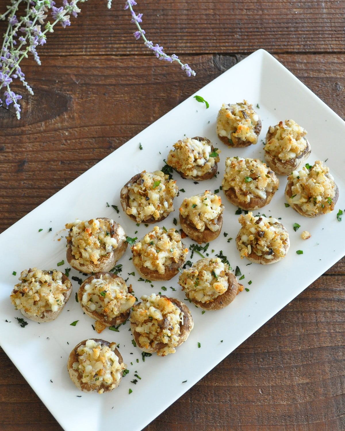 stuffed mushrooms on a white platter next to a bundle of lavender