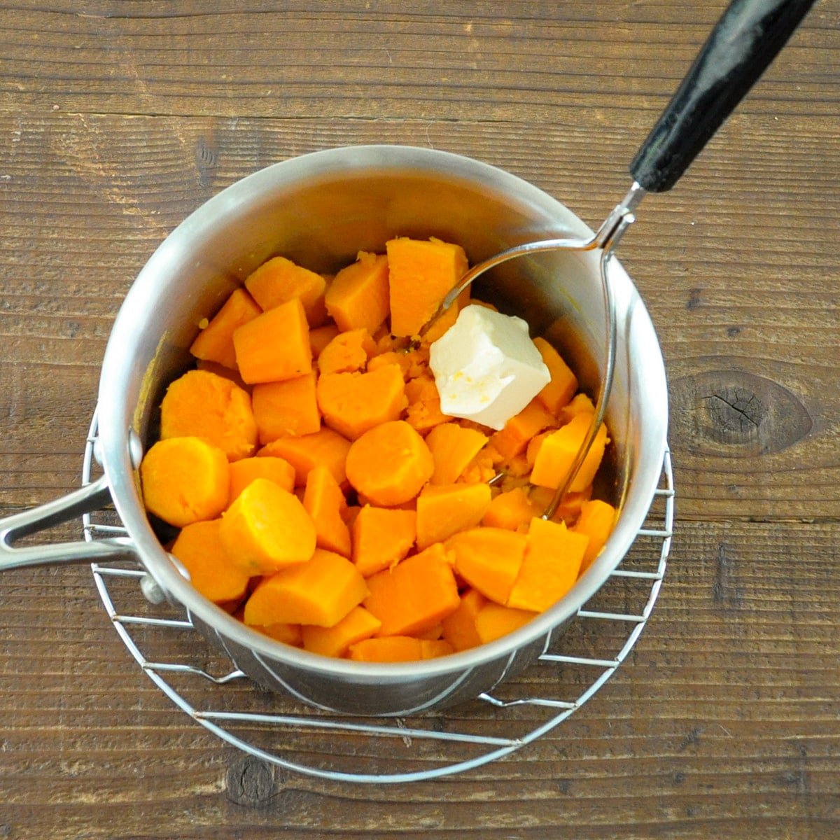 cut up sweet potatoes in a pan with some butter and a masher