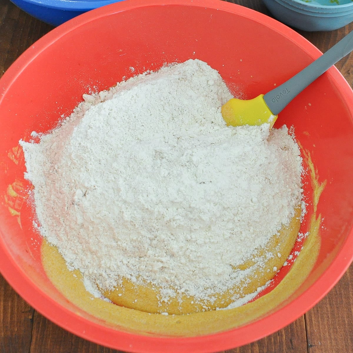 Flour mixture added on top of the pumpkin batter in a red bowl, with a rubber spatula.
