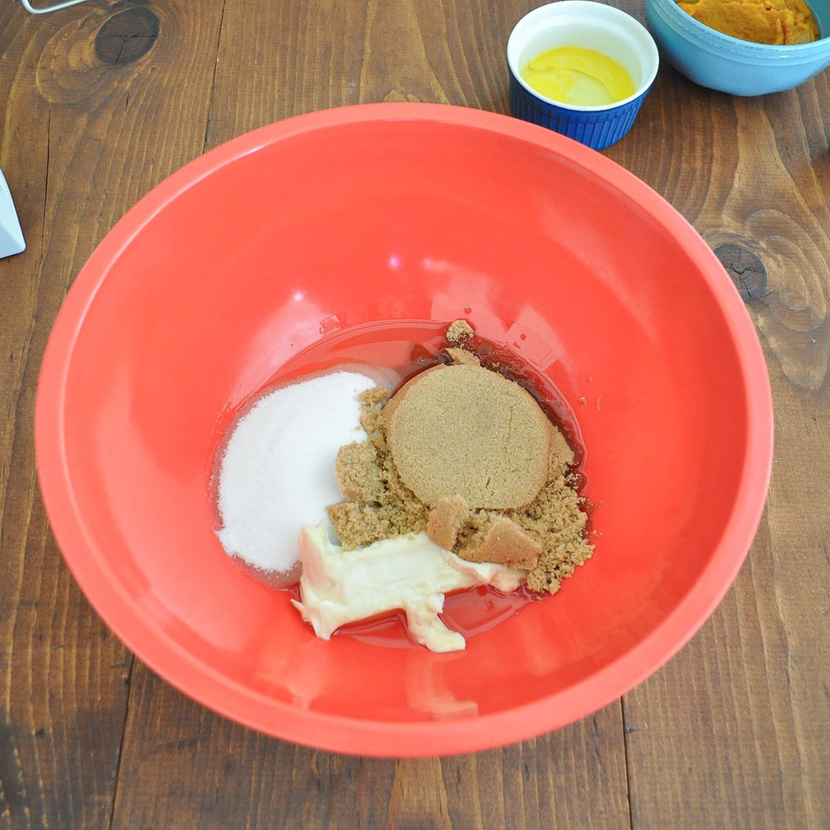 Butter, granulated sugar, brown sugar, and canola oil in a red mixing bowl before mixing.