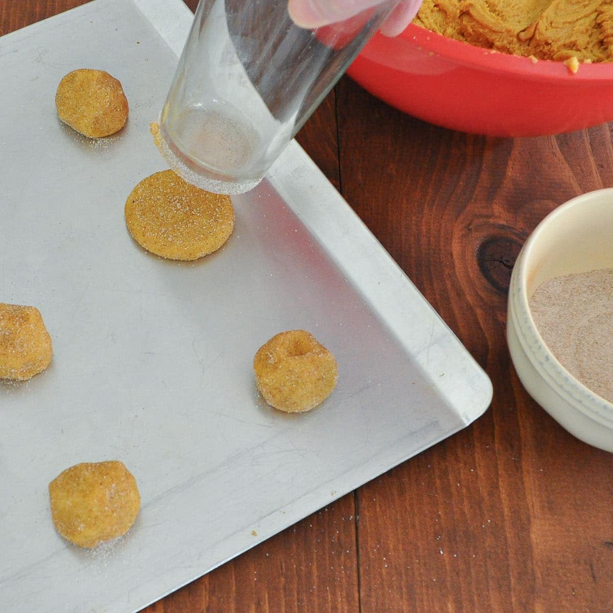 A sugared drinking glass beside a freshly flattened cookie, with more dough balls waiting on the sheet.