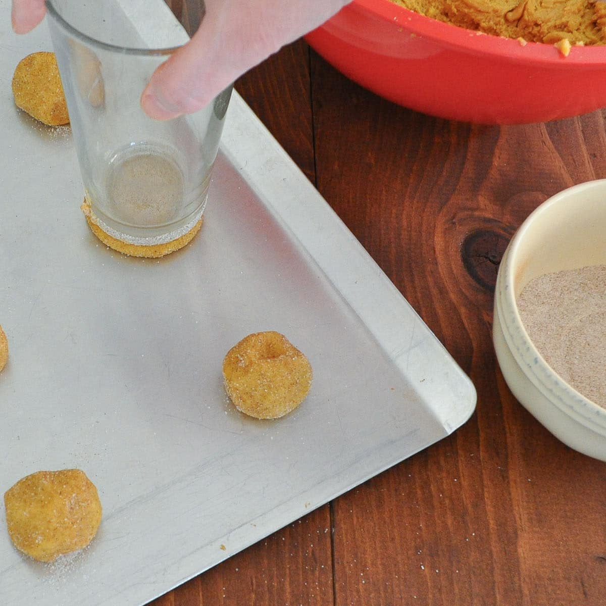 A hand pressing a sugar-coated dough ball flat with the bottom of a drinking glass.