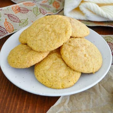 Pumpkin snickerdoodle cookies piled on a speckled white plate with a fall leaf ribbon in the background.