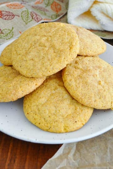 Pumpkin snickerdoodle cookies piled on a speckled white plate with a fall leaf ribbon in the background.