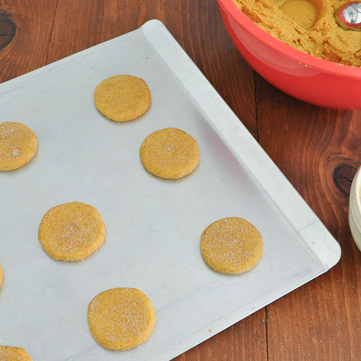 Flattened, sugar-coated pumpkin cookie dough rounds on a cookie sheet, ready to bake.