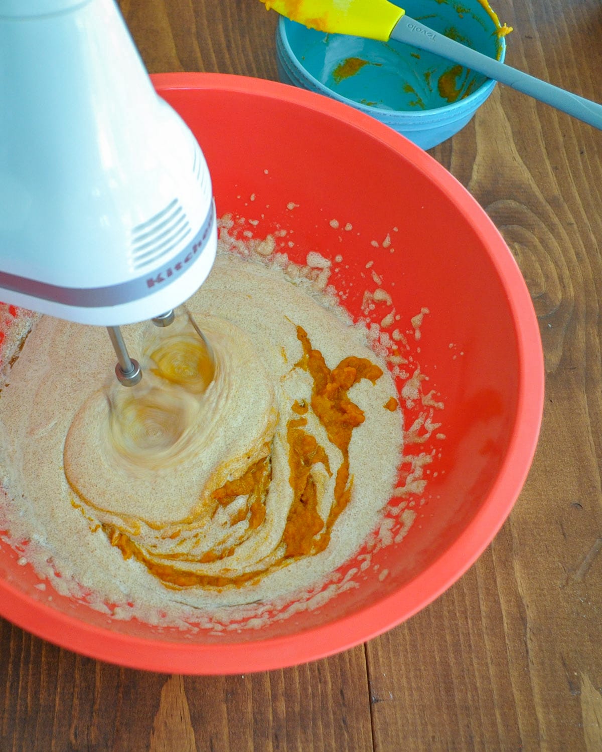 pumpkin puree being added to butter, oil, and sugar cookie mixture in a large bowl