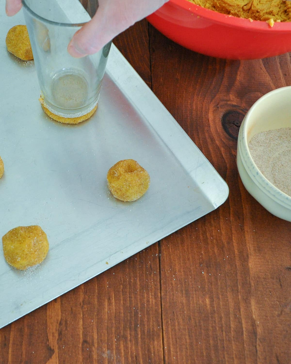 a drinking glass being used to flatten cookie dough on a cookie sheet