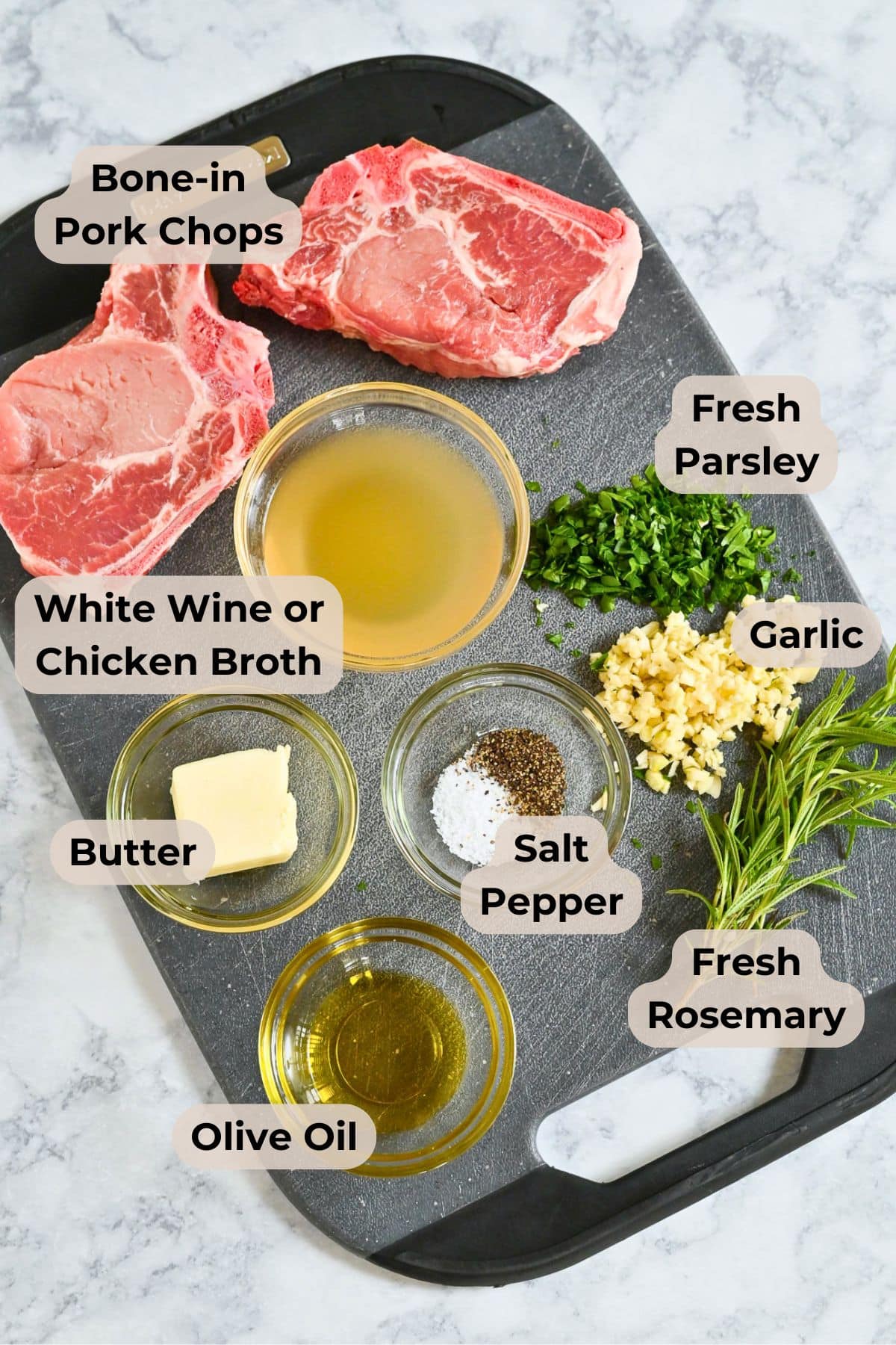 Labeled ingredients on a cutting board: pork chops, broth, parsley, garlic, rosemary, olive oil, butter, salt, pepper-for making Pork Chops with Garlic White Wine Sauce.