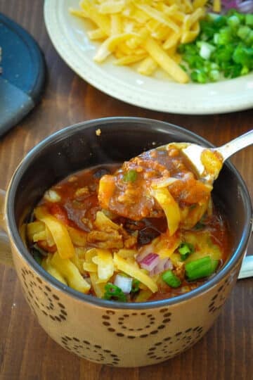 a large cup of chili covered in cheese and onions