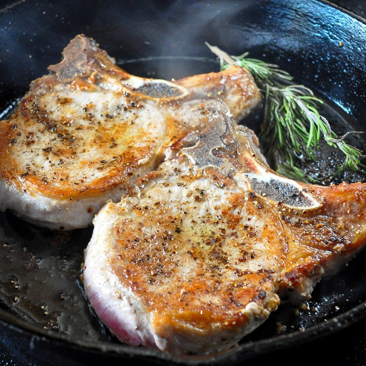 browned pork chops in a hot skillet with rosemary