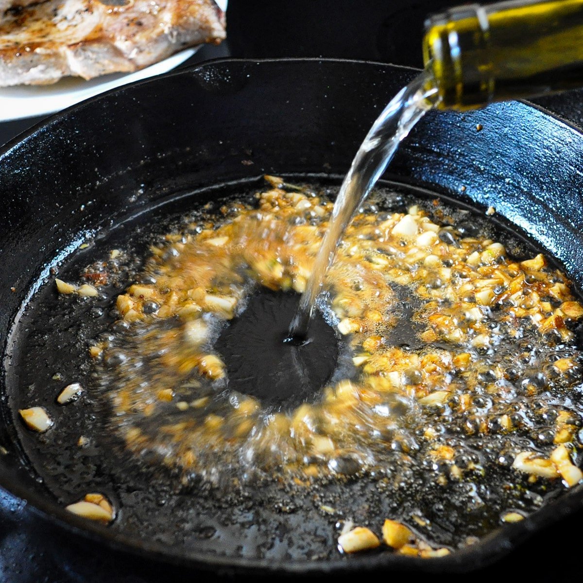 garlic and white wine being poured in a hot skillet
