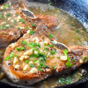 2 pork chops in a skillet browned and topped with garlic