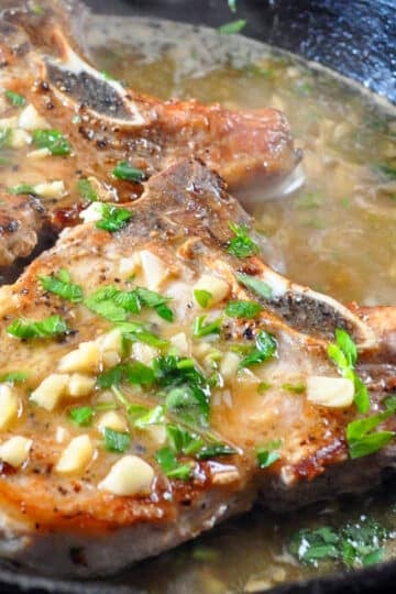 2 pork chops in a skillet browned and topped with garlic
