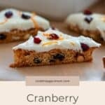 A closeup of Cranberry Bliss Bars topped with white icing, cranberries, and orange zest on parchment paper.