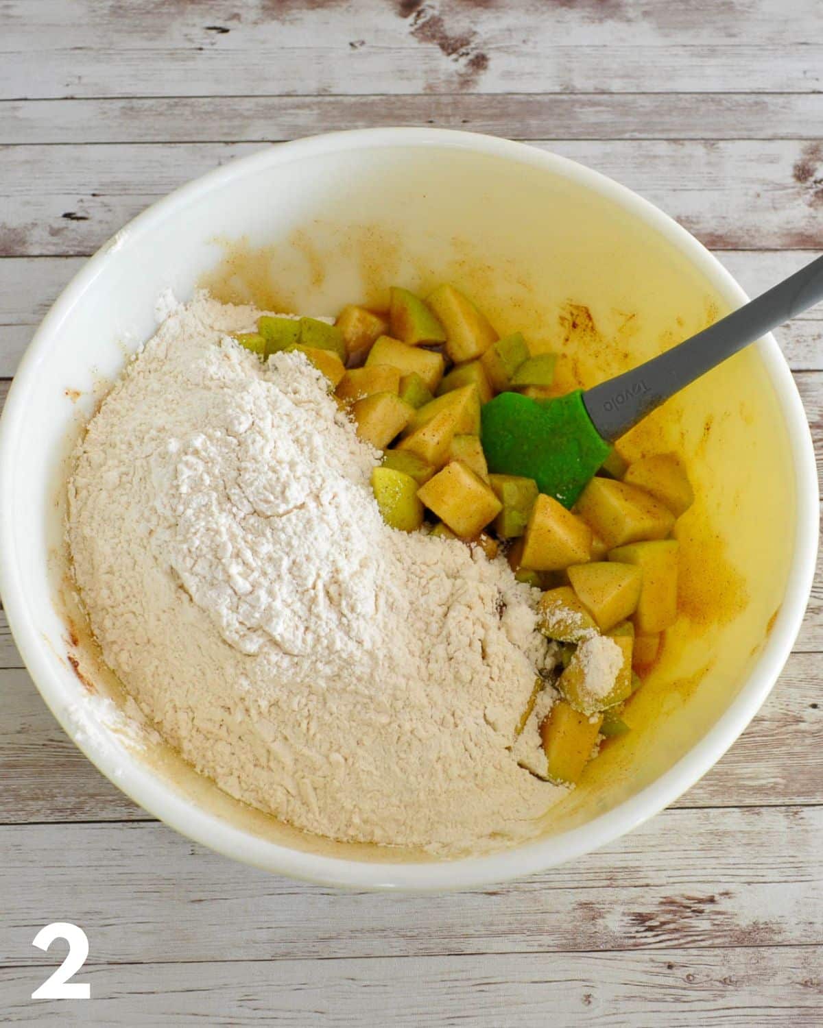 Flour and other dry ingredients added to cubed apples in a large mixing bowl. 