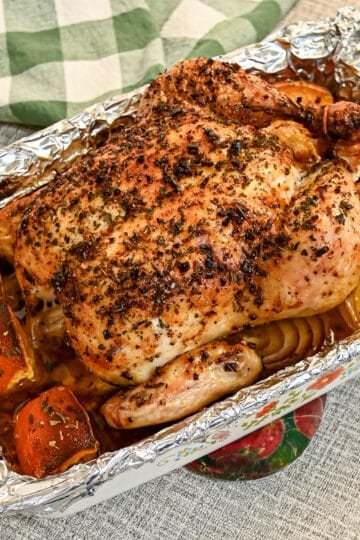 A roasted whole chicken with herb crust and orange wedges in a foil-lined baking dish.